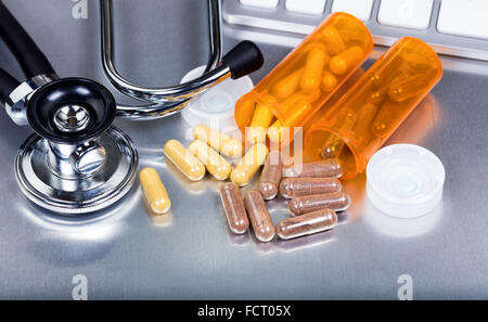 Close up of capsules spilling out of containers with stethoscope and keyboard in background on stainless steel surface. Stock Photo