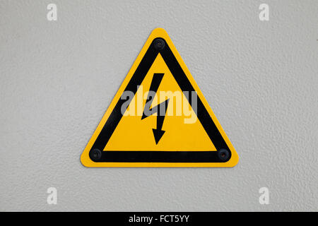 High voltage triangle warning sign mounted on gray metal wall Stock Photo