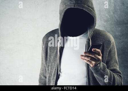 Faceless hooded person using mobile phone, unrecognizable male with smartphone, identity theft and technology crime concept. Stock Photo