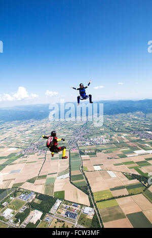 Two freefly skydivers are training the sit-flight together. Thereby they fly with over 120 mph speed in the blue sky over fields Stock Photo