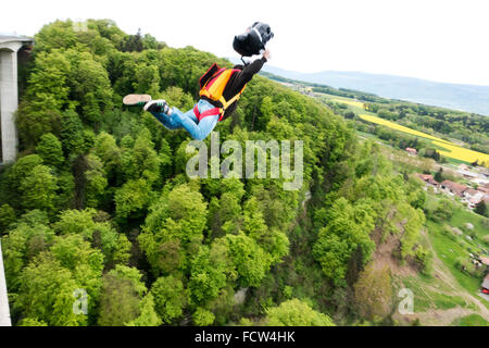 Man is exiting from a bridge with his BASE jumping equipment. With the pilot-chute in his hand he'll forces the opening process. Stock Photo