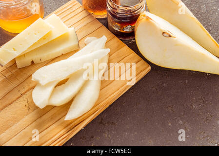 A composition of italian cheese pecorino slices with jams and pears on a wooden chopping board Stock Photo