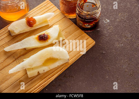A composition of italian cheese pecorino slices with jams and pears on a wooden chopping board Stock Photo