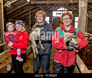 Family inside a barn, with sisters holding lambs, Iceland Stock Photo