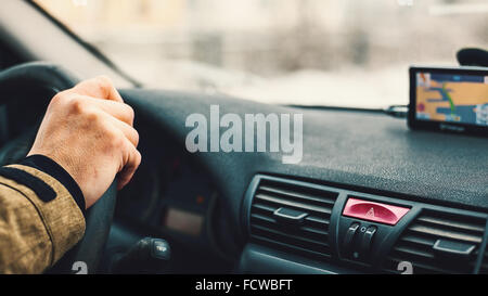 Details of a man's arm on vehicle wheel, navigation device in blurry background. Stock Photo