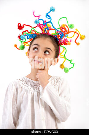 Thoughtful pretty little girl with a colorful headdress of streamers holding her finger to her face as she looks pensively into Stock Photo