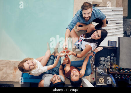Overhead view of group of friends toasting at party by a swimming pool and looking up at camera smiling. Multiracial young peopl Stock Photo