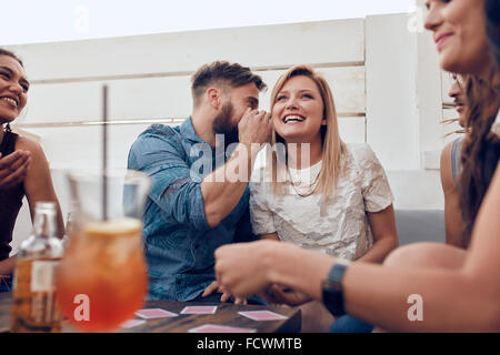 Young people sitting together in a party. Man whispering something in woman's ears. Sharing a secret. Stock Photo