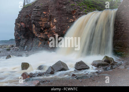 Springtime Nova Scotia coastline in June.   Waterfalls from cliff onto rocky pebble beach. Stock Photo