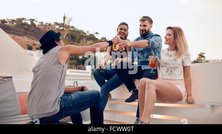 Shot of young people sitting together having wine. Group of multiracial friends toasting at party outdoors. Men and women enjoyi Stock Photo