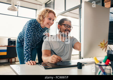 Two young male and female designers working together, with man editing artwork using graphics tablet and a stylus. Creative peop Stock Photo