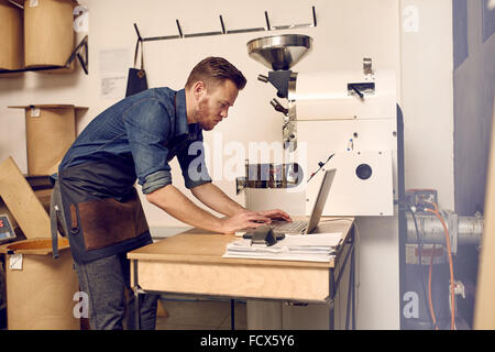 Modern coffee roaster using his laptop alongside a modern roasti Stock Photo