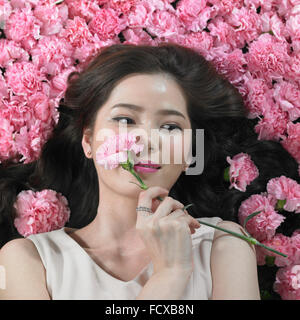 High angle of woman lying on carnation flowers and holding one of them on her face and looking down Stock Photo