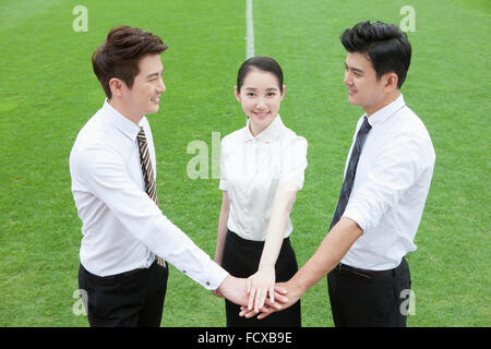 High angle of two business men looking at each other and woman staring forward all putting their hands together on grass field Stock Photo
