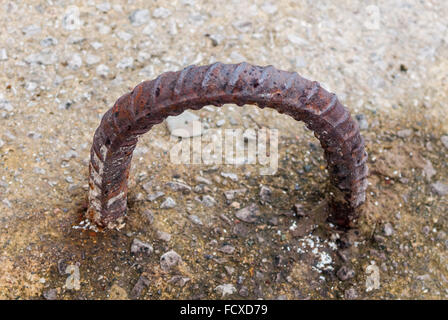 Rusted dirty old metal rebar loop with both ends embedded in cement. Stock Photo