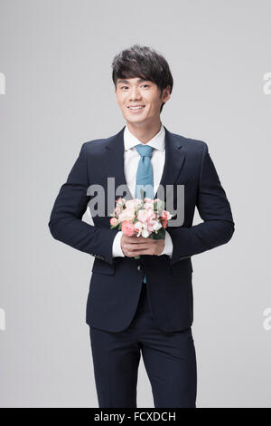 Man in black suit and blue tie holding flowers in his hand and smiling Stock Photo