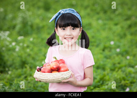 Young girl holding a basket with apples and smiling with the background of green farm Stock Photo