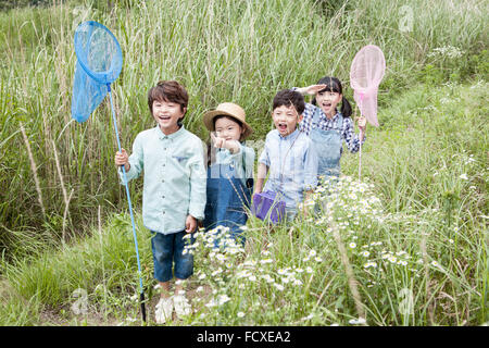 Four kids having fun with butterfly nets in the tall grass field Stock Photo