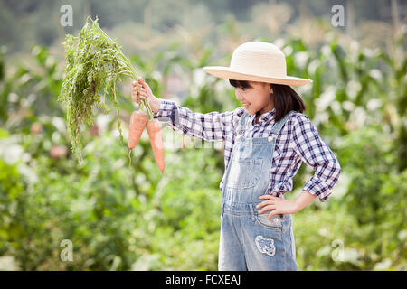 Girl in a straw hat holding carrots at field Stock Photo