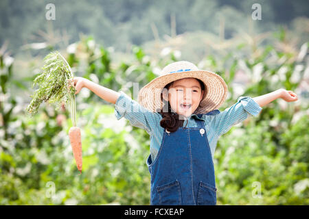 Girl in a straw hat opening her arms wide with a carrot in one hand Stock Photo