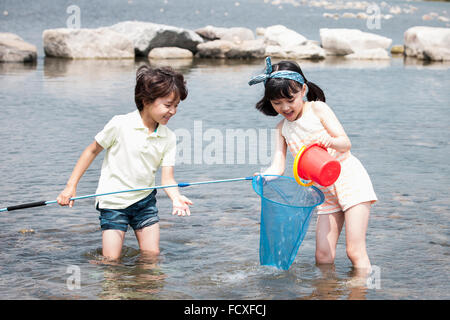 Boy and a girl standing in the water and holding a scooping net for fishing and a bucket enjoying their summer vacation Stock Photo