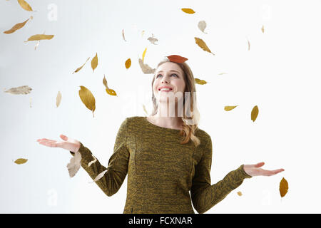Portrait of young smiling woman holding hands up and looking up in falling leaves Stock Photo