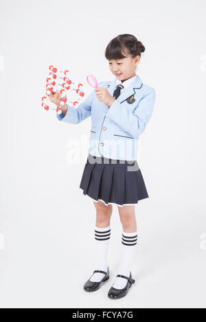 Elementary school girl in school uniforms standing and holding a molecular structure and observing it through a magnifying glass Stock Photo