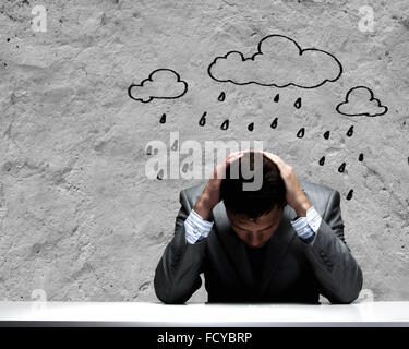 Depressed young businessman sitting wet under rain Stock Photo