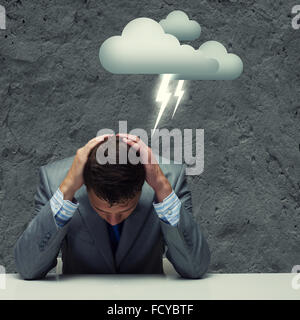 Depressed young businessman sitting wet under rain Stock Photo