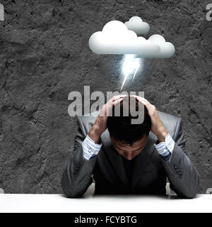 Depressed young businessman sitting wet under rain Stock Photo