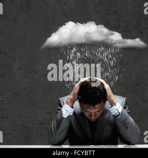 Depressed young businessman sitting wet under rain Stock Photo