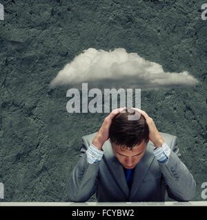 Depressed young businessman sitting wet under rain Stock Photo