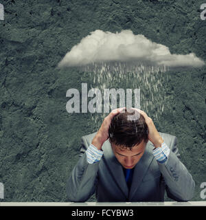 Depressed young businessman sitting wet under rain Stock Photo