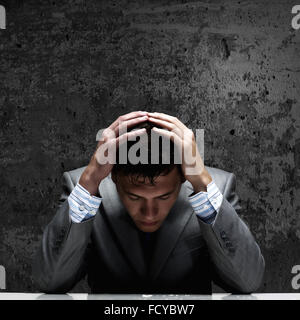 Depressed young businessman sitting wet under rain Stock Photo