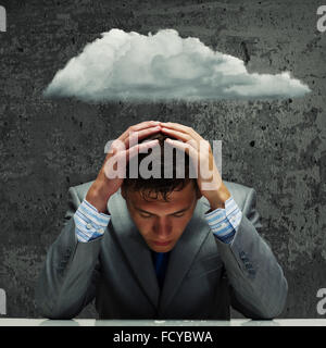 Depressed young businessman sitting wet under rain Stock Photo