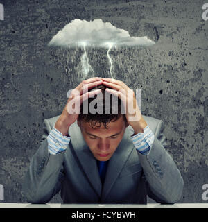 Depressed young businessman sitting wet under rain Stock Photo