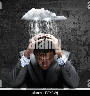 Depressed young businessman sitting wet under rain Stock Photo