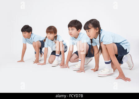 Four elementary school students in sportswear kneeling down to run looking up Stock Photo