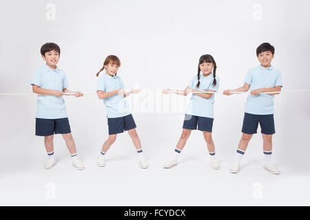 Four elementary school students in sportswear doing tug of war into two teams Stock Photo