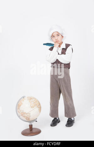 Boy in classical scholar style holding a feather pen and standing behind a globe with the gesture of thinking Stock Photo