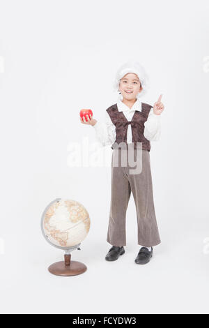 Boy in classical scholar style holding an apple with his finger up and standing behind a globe staring forward with a smile Stock Photo