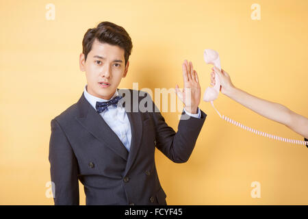 Man in suit and bow tie in frowning face putting his palm against the phone held by a hand Stock Photo