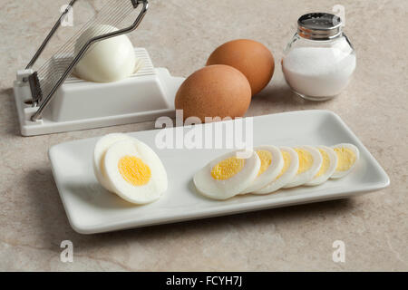 Hard boiled egg in slices on a dish with an egg slicer and salt on the background Stock Photo