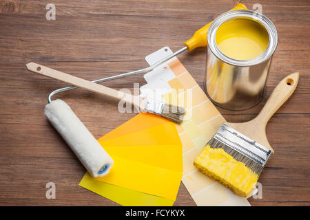 High angle of yellow paint and paint brush dipped in yellow paint with yellow color schemes and paint roller on wood background Stock Photo