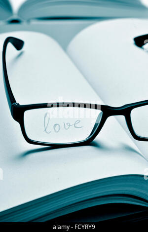 the word love handwritten in a notebook seen through the lens of a black plastic-rimmed eyeglasses, in duotone Stock Photo