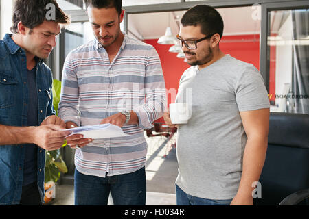 Group of young creative professionals having a meeting in office, going through some documents together. Creative team of three Stock Photo