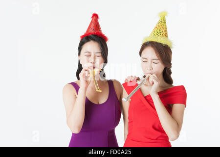 Two women in party hat and dress blowing a party horn each with their eyes closed Stock Photo