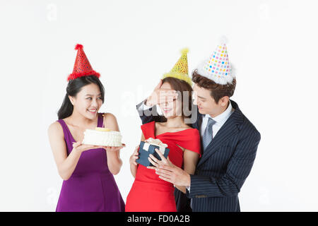 Three young adults celebrating the woman's birthday with a cake and a gift all in party hat Stock Photo