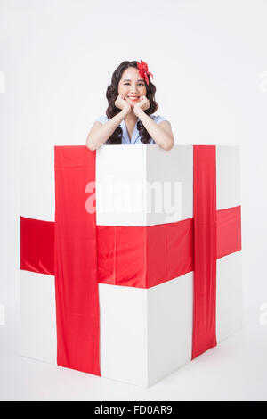 Woman in retro style with ribbon on her hair placed inside of a gift box with red ribbon Stock Photo