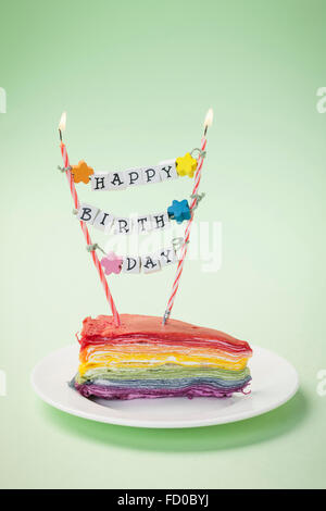 Colorful piece of cake on a plate with the candles and message of Happy Birthday Stock Photo